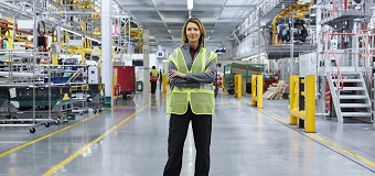 A female manager stands in a hi-vis vest on a factory floor